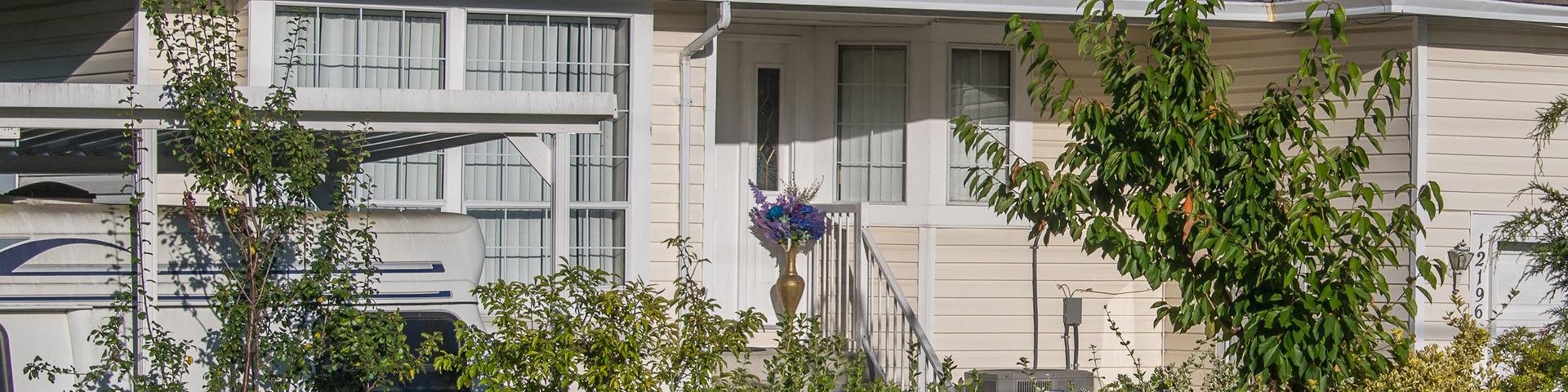 Greenery rests in front of and beside the stairs to the front door of a white house.