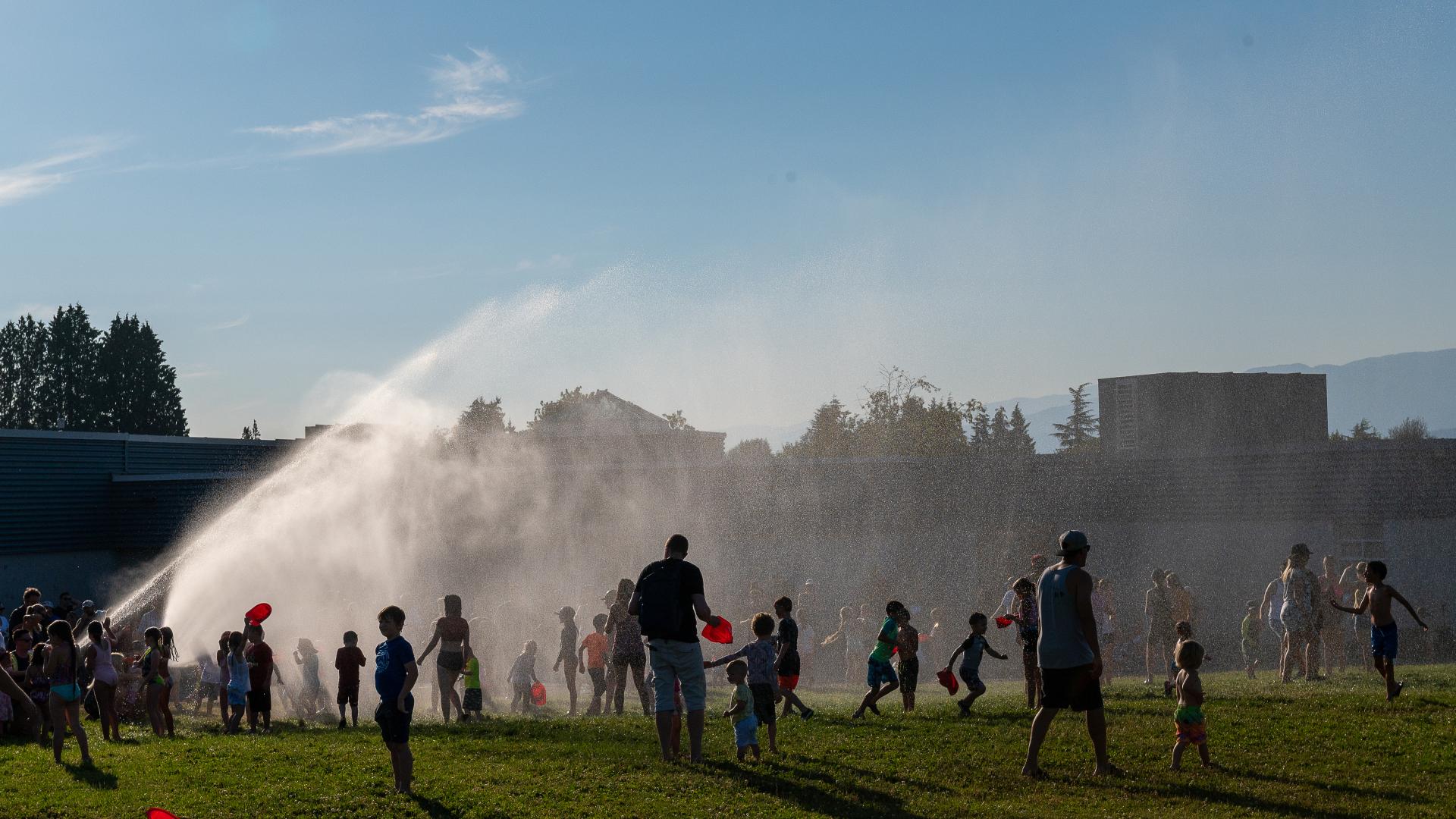 A group of people enjoy the spray from a fire hose on a hot day during an exhibition put on by Maple Ridge Firefighters.