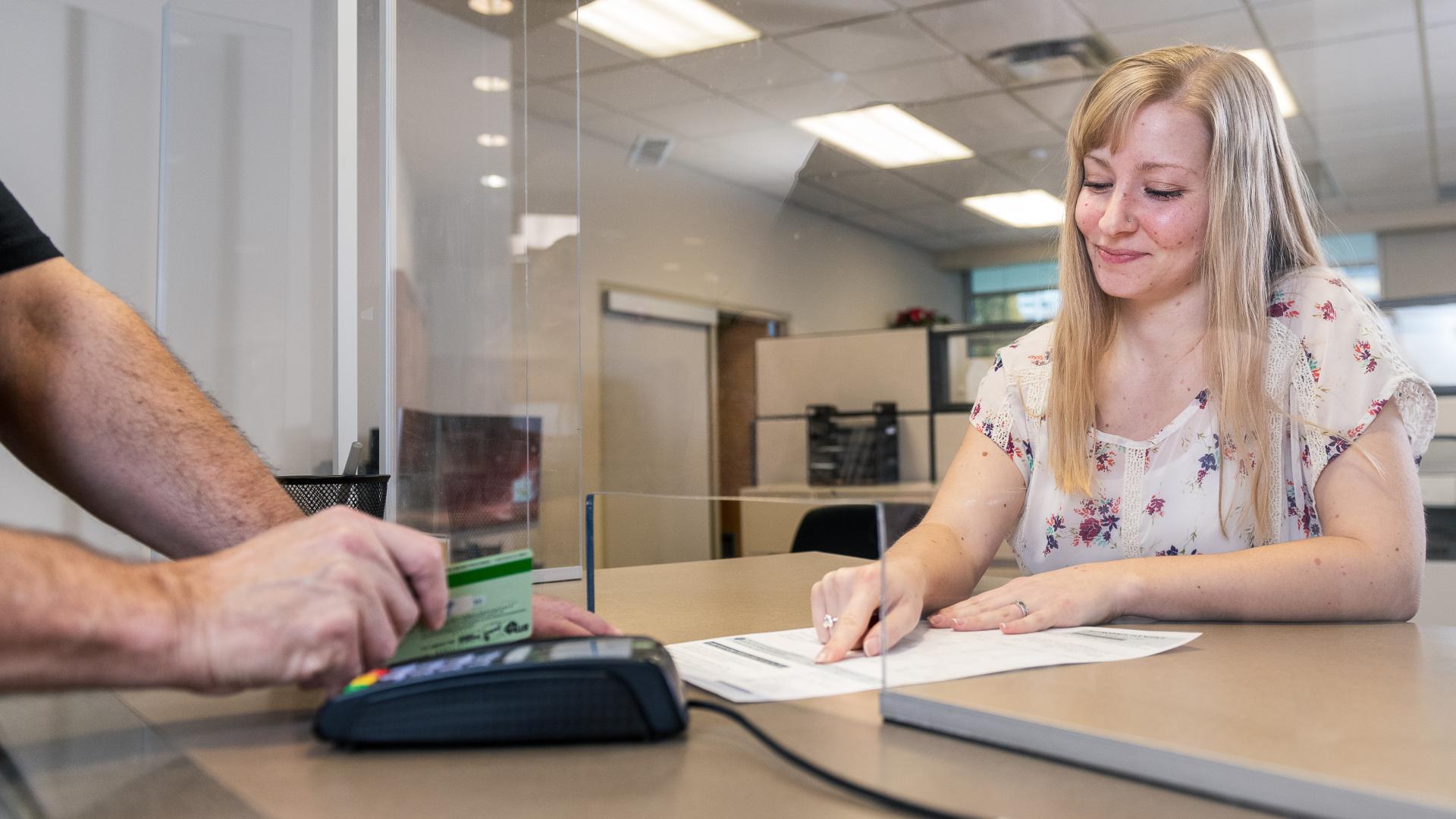 A worker in City Hall shows an individual the final balance of their bill so that they can pay using the credit card and point of service machine in front of them.