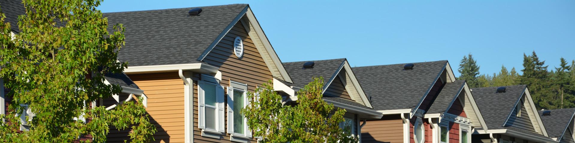 A line of townhomes and street trees sit against a bright blue sky.