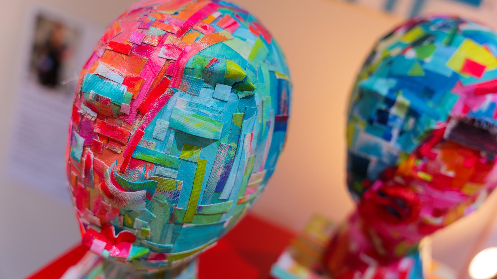 Blue and red painted paper head sculptures sit displayed on a red clothe on a table.