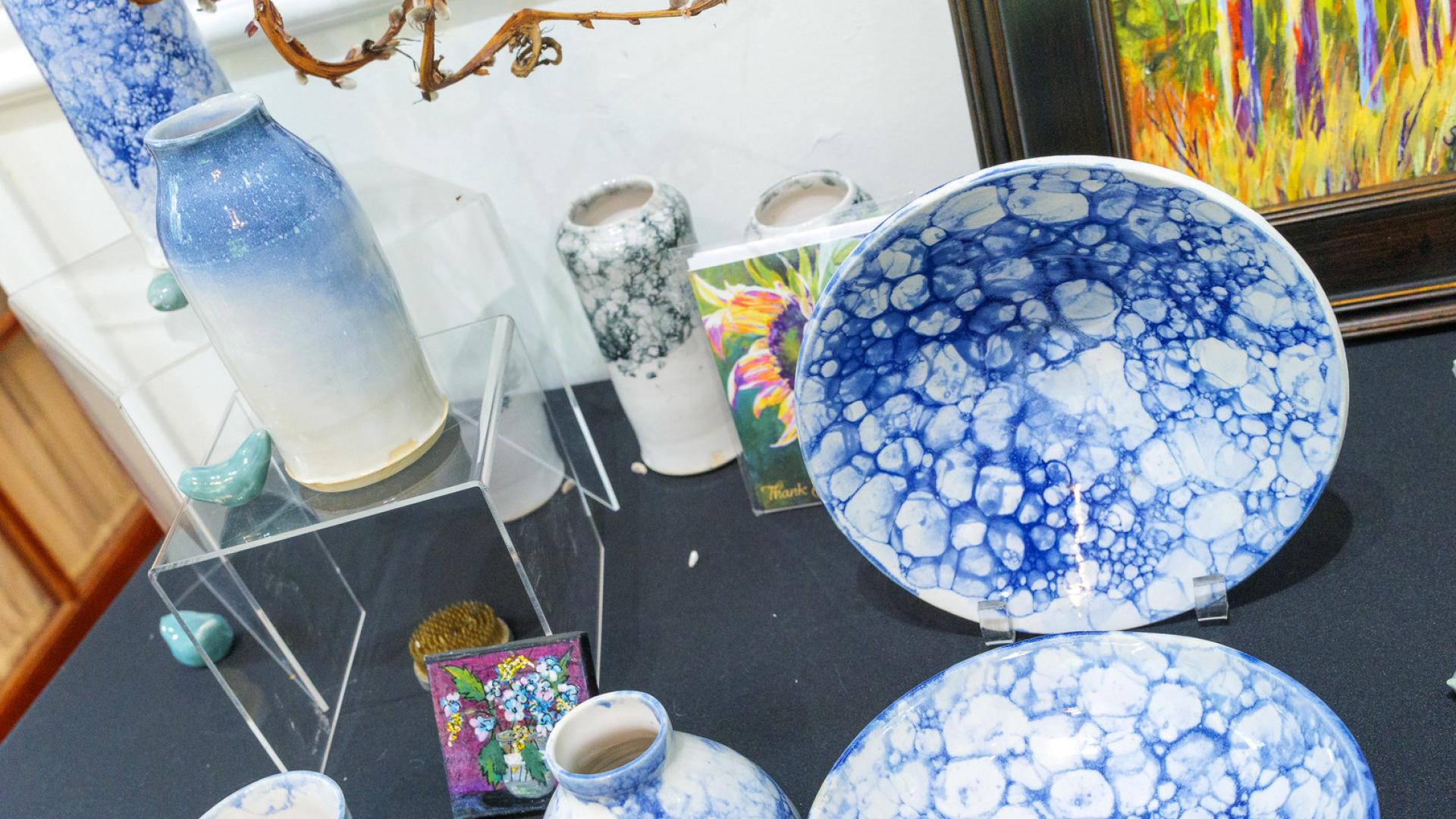 Blue bubble-glazed ceramic plates and vases sit next to paintings and other artworks.