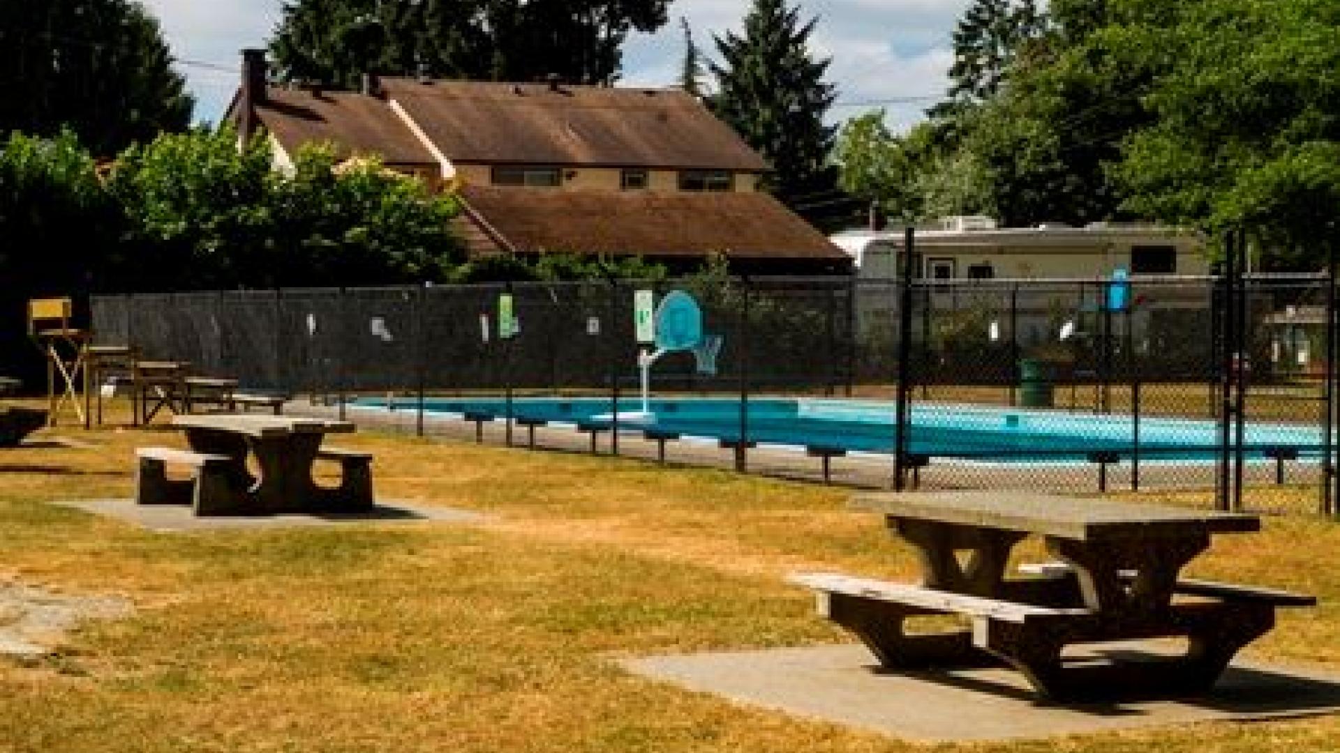 A fenced in pool. Outside the fence is a grassy area with two picnic tables.