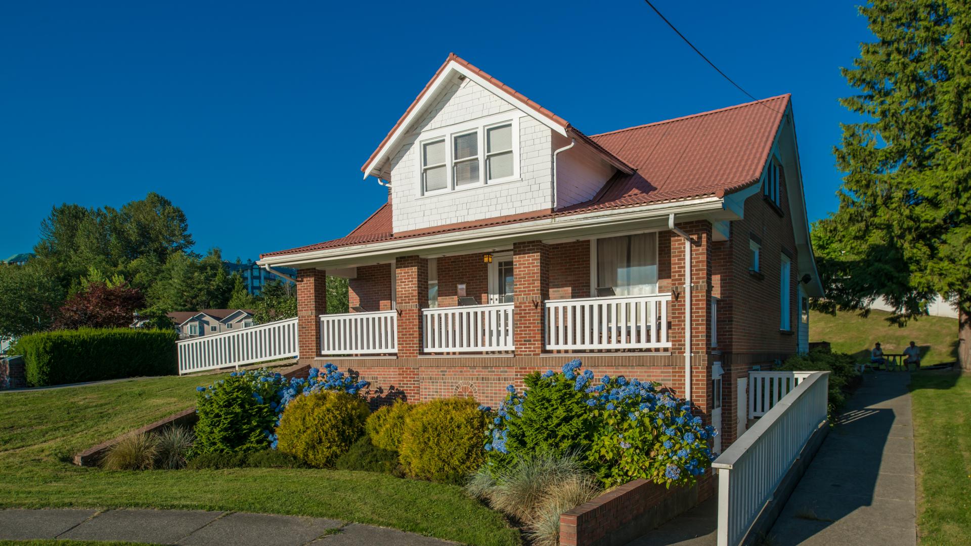Exterior of Haney Brickyard office. There is a small brick building on a plot of land. The building is surrounded by greenery and shrubs.