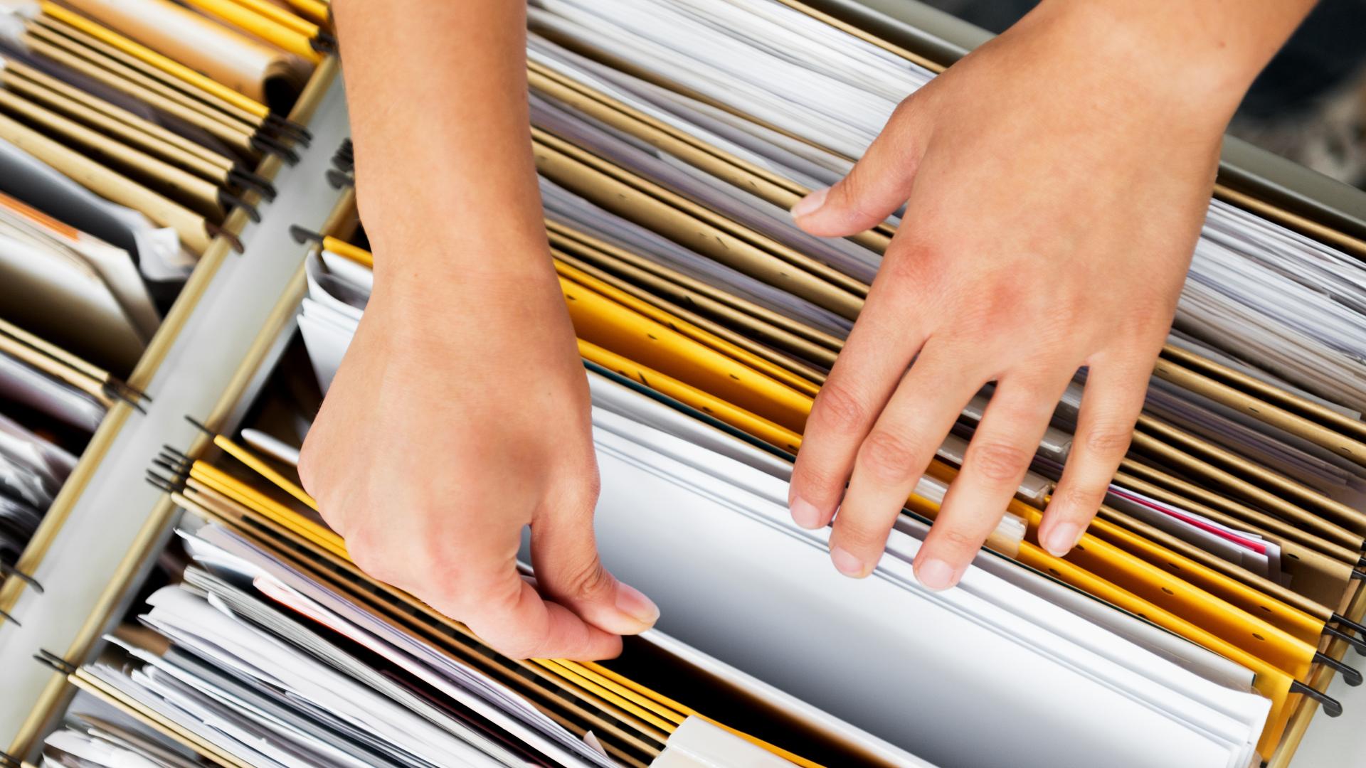 A pair of hands pull apart file folders to grasp a specific document.