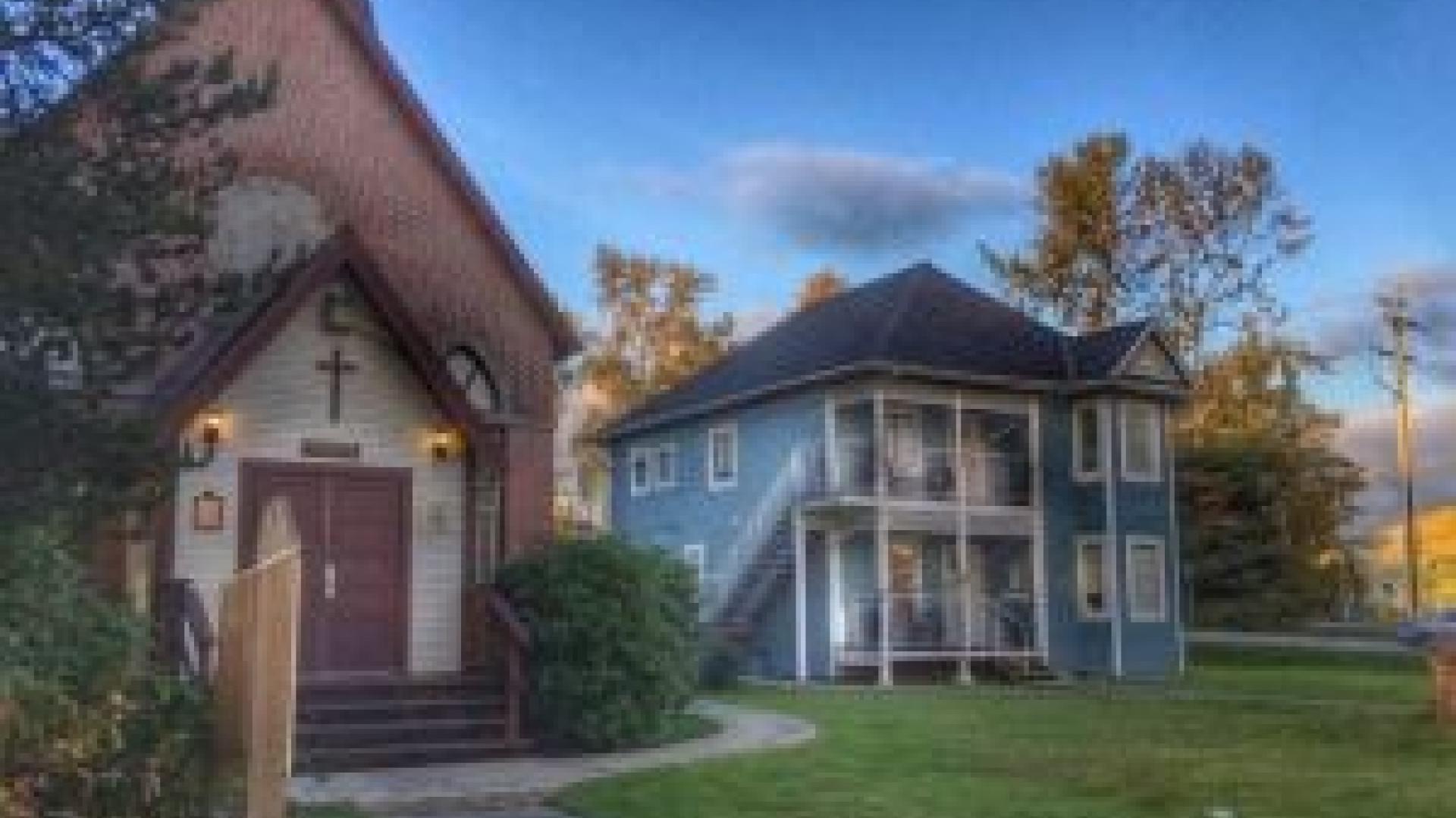 Exterior of Manse and St Andrews Church. The Manse building is a multi-story blue wooden building. 