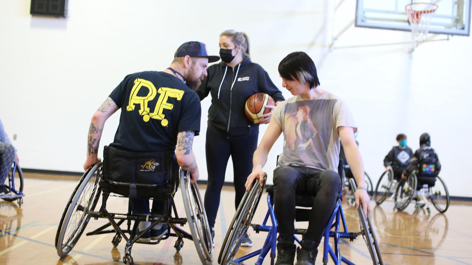 A man and a teen in wheelchairs facing each other on a basketball court