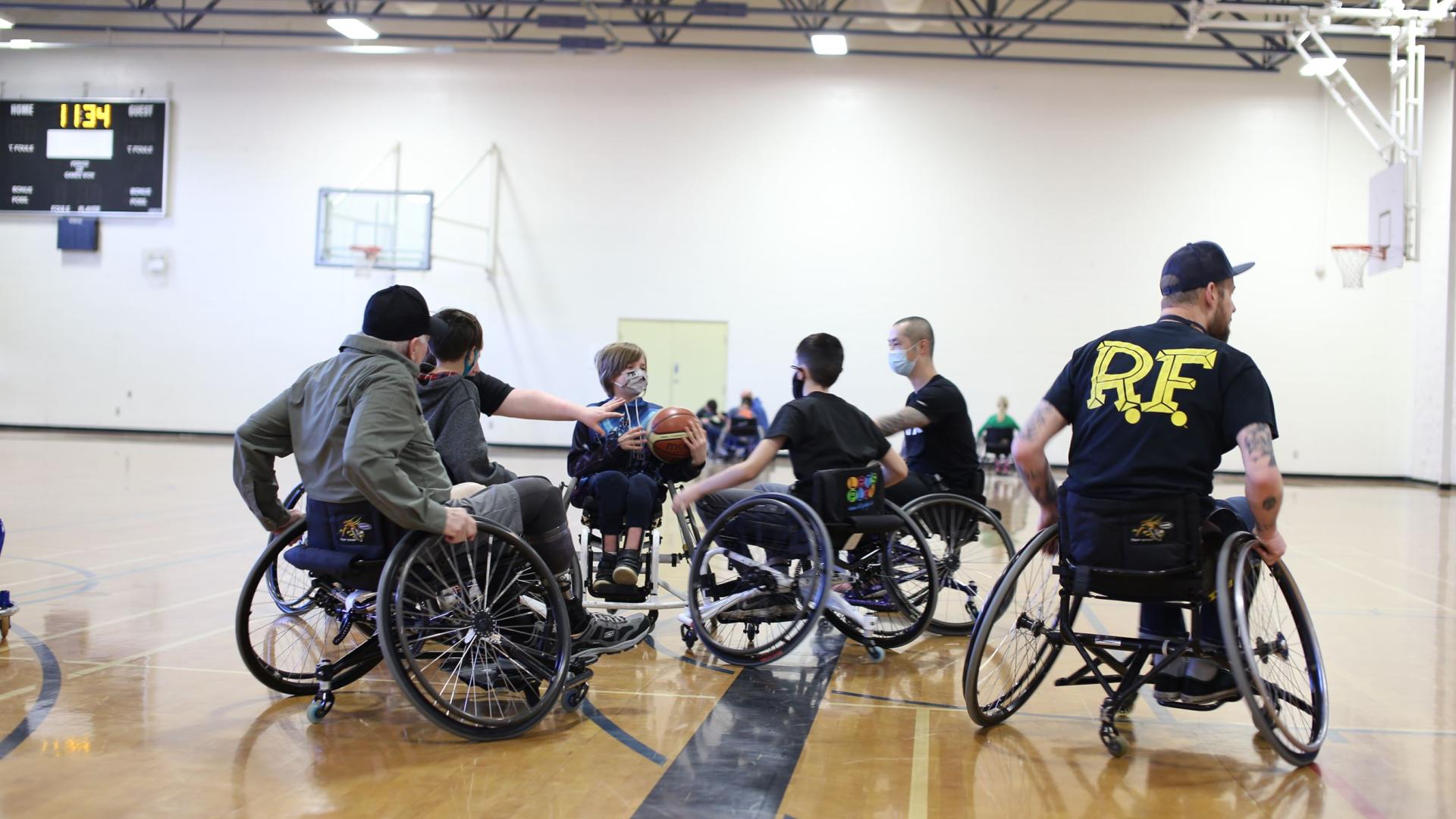 A group of teens and adults in wheelchairs playing basketball