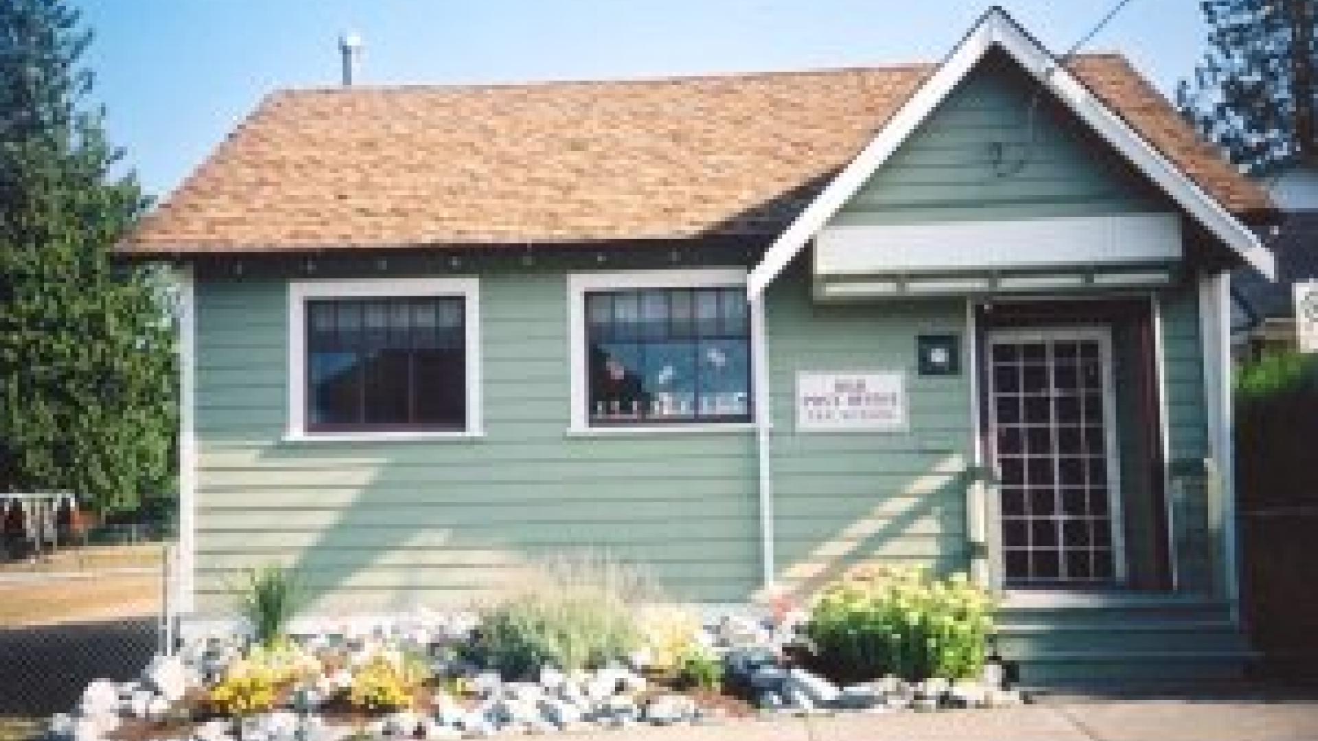 Exterior of old post office. The post office is a small building painter in a light lime green. The front of the building has a small floral garden.