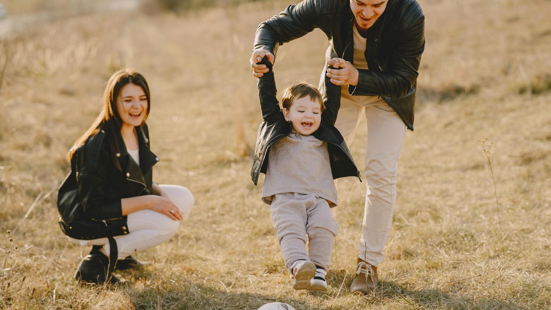 Parents in a Field Holding The Hands of Their Young Child