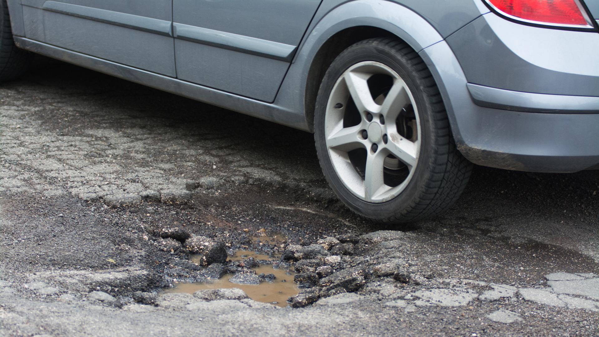 A blue-grey four-door sedan rests next to a pothole.
