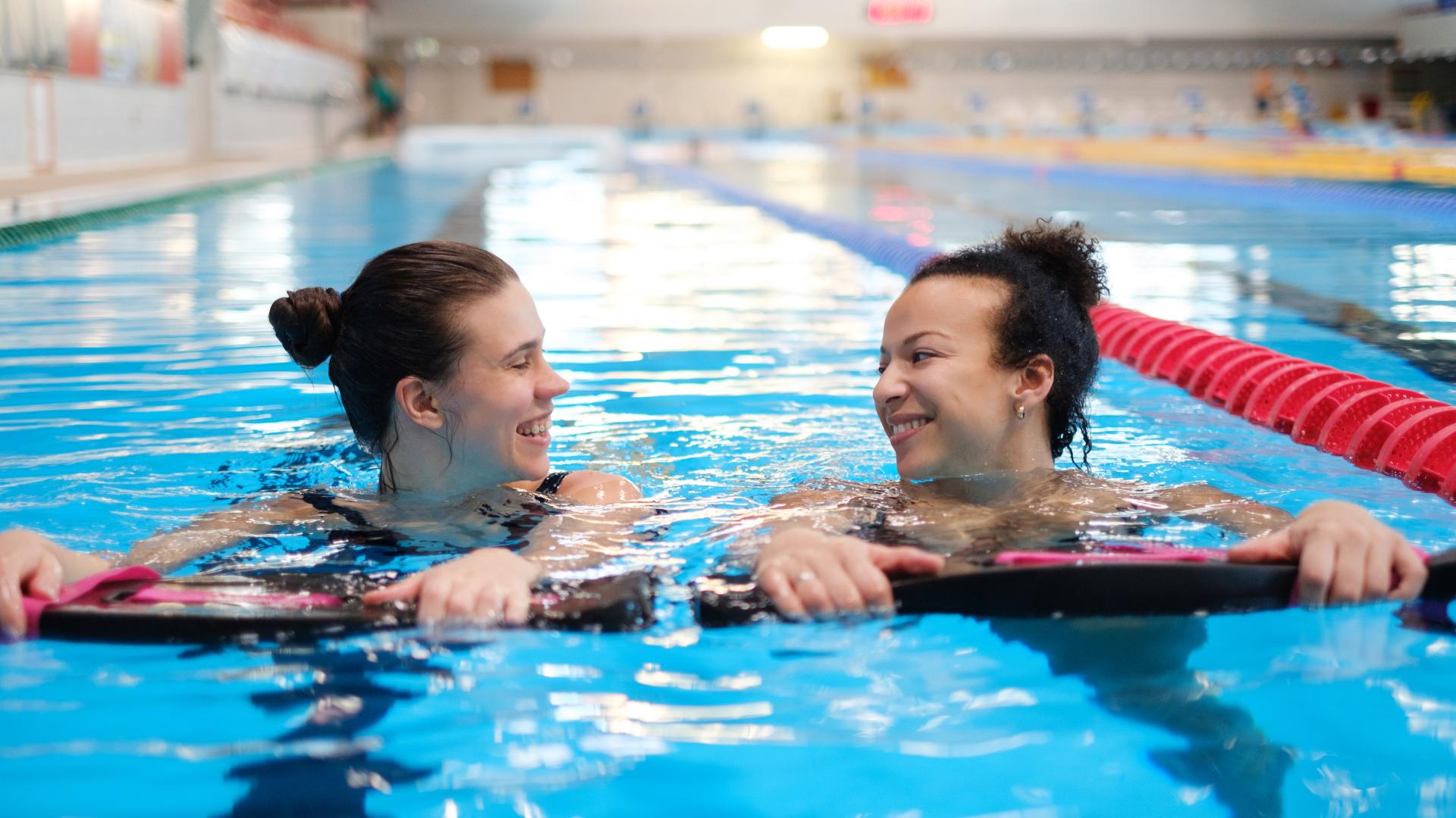 Two women smile at each other while swimming in a pool.