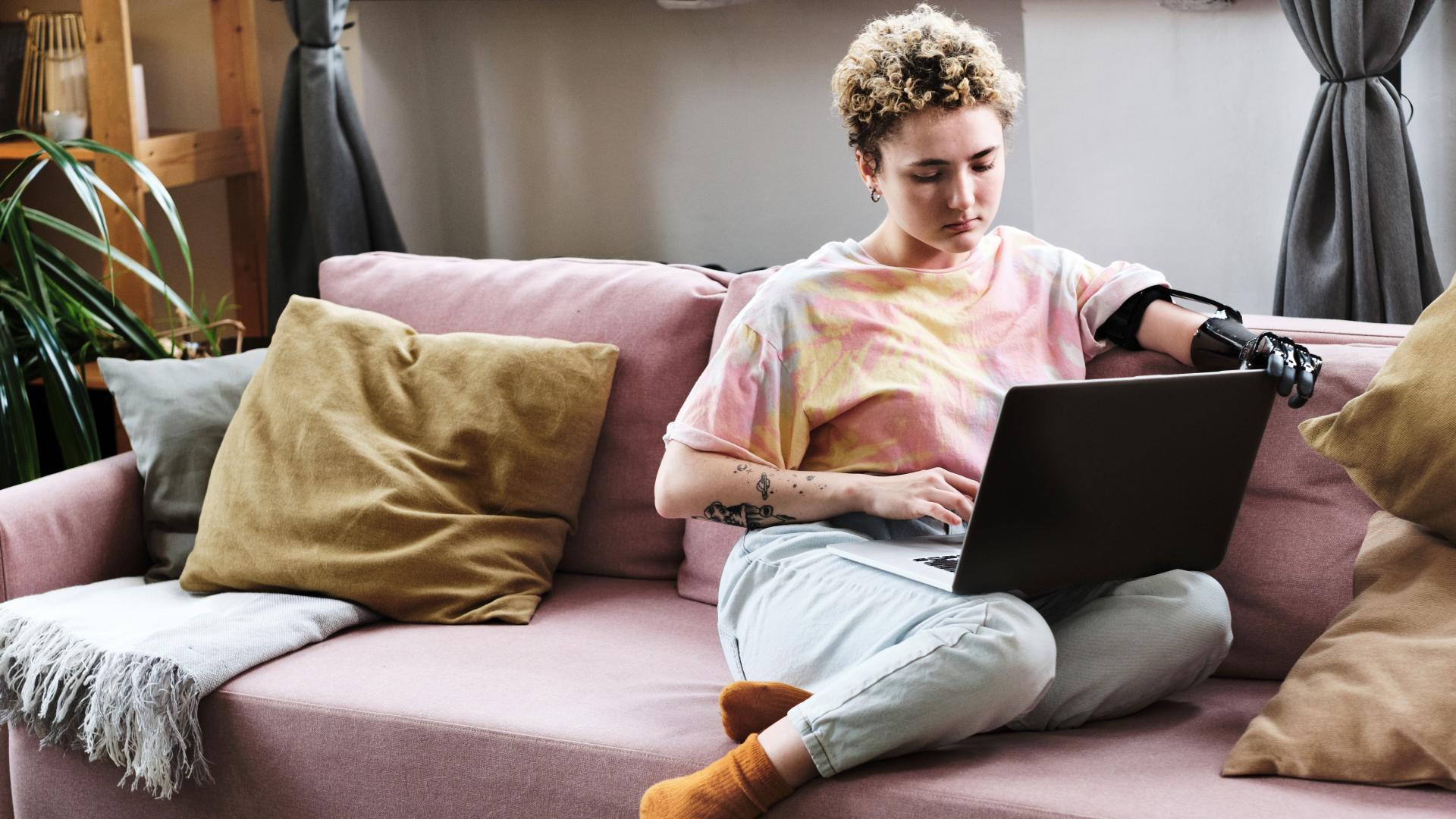 A woman with a prosthetic arm sits on her sofa while using a computer.