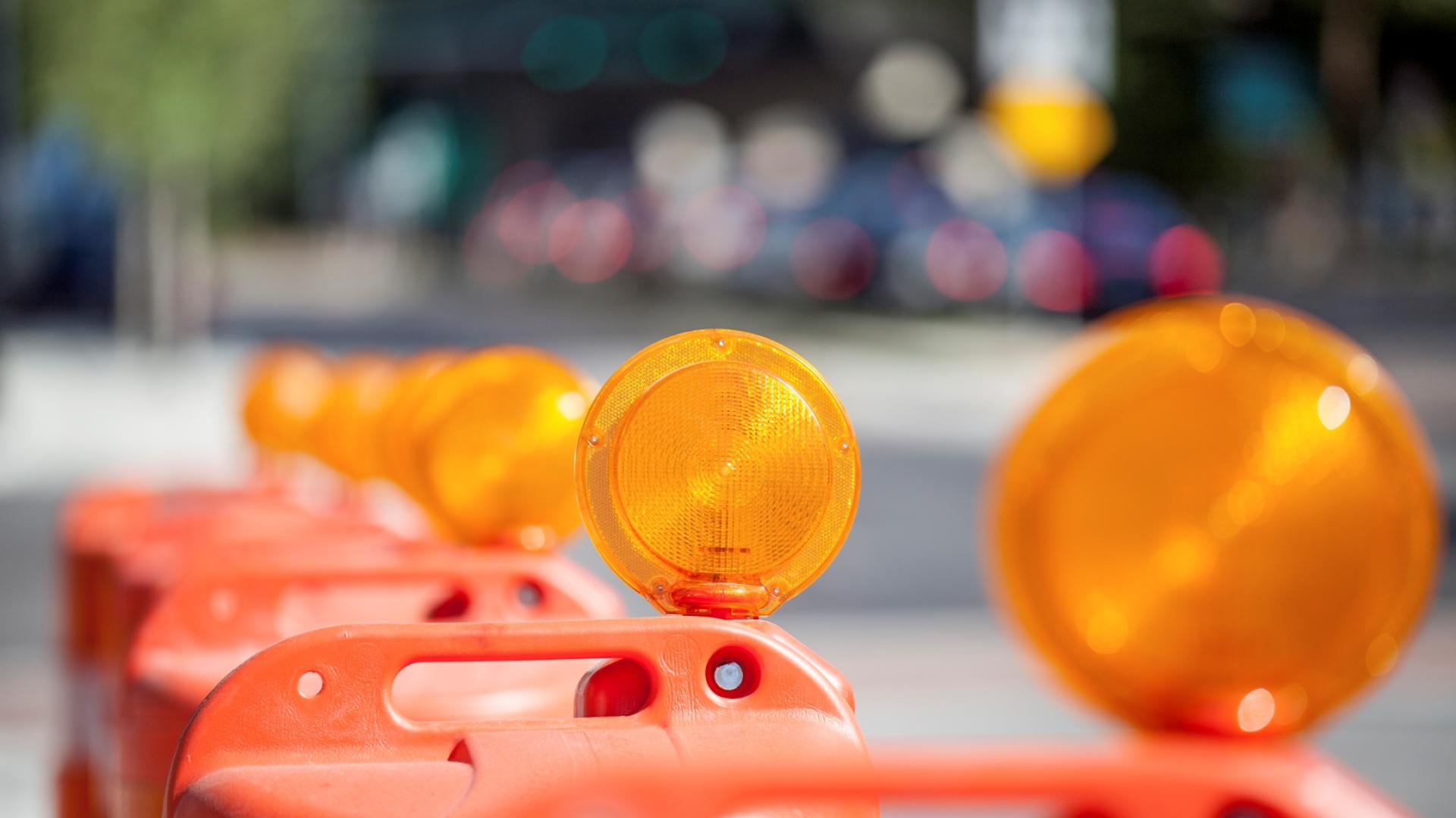 A line of orange pylons with high-visibility reflectors line a street, separating traffic from construction.