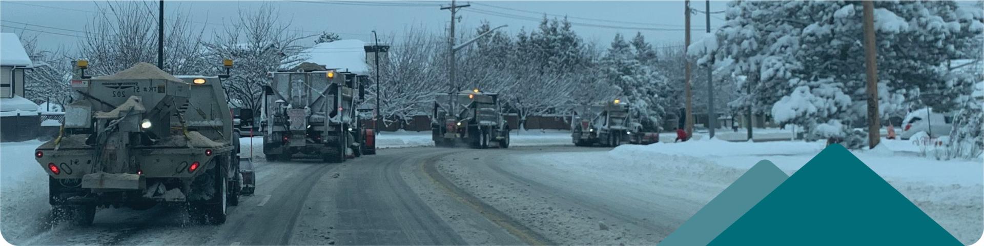 A line of snow removal trucks travels down a street.