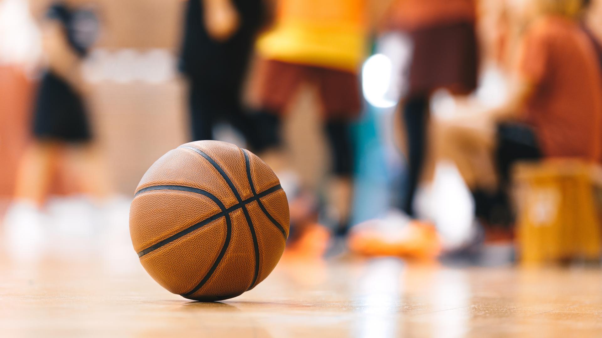 Basketball in a Gymnasium with Group Behind It