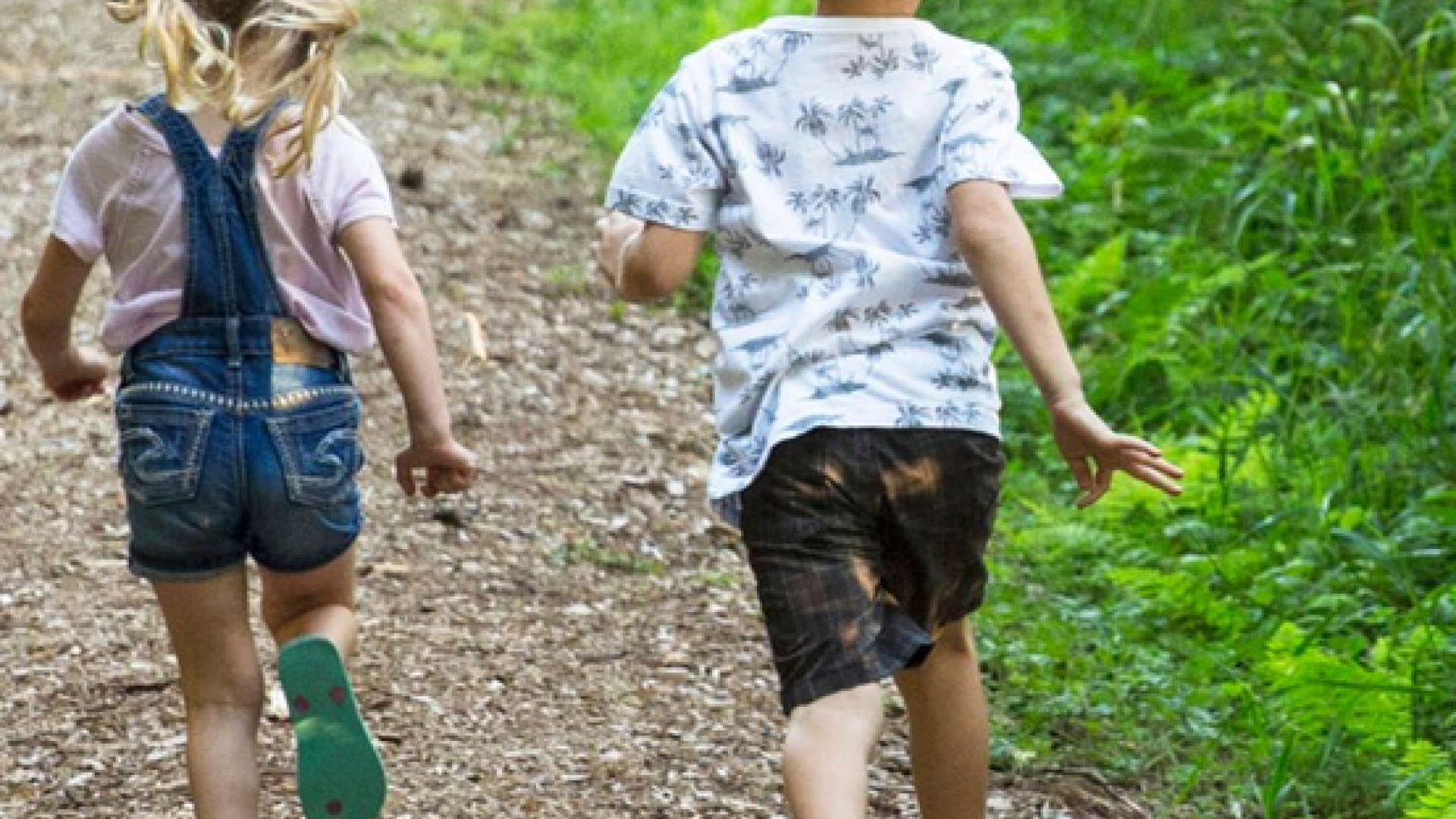 a young boy and girl running on a wood chip trail (picture taken from behind)